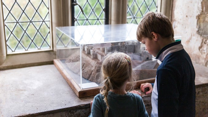 Two children look at a model castle in a clear case on a castle window sill inside the castle